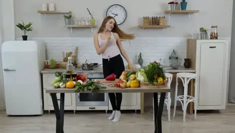 Happy vegan girl with slim waist dancing singing in kitchen Raw vegetable nutrition diet concept