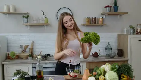 Young girl dancing having fun and cooking salad with raw vegetables Throwing pieces of lettuce