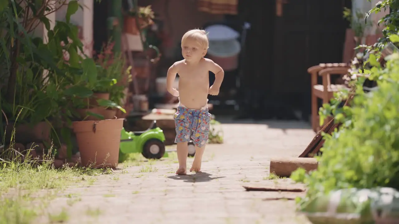 A blonde-haired fair-skinned toddler boy runs happily in the yard of the rural house