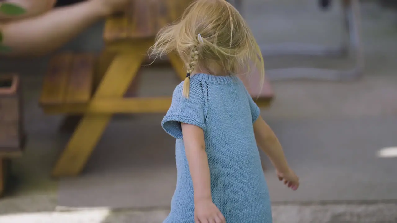 A little blonde-haired girl in a blue dress dances and spins joyfully