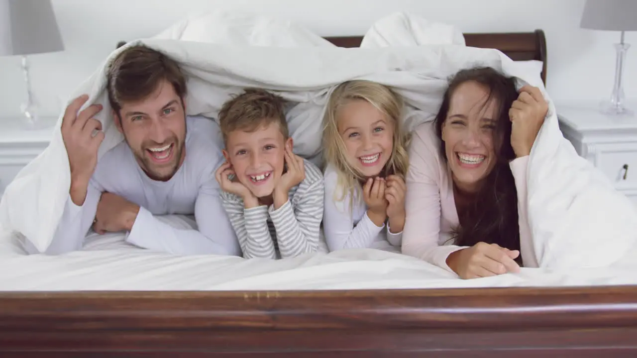 Family lying together under blanket in bedroom at home 4k