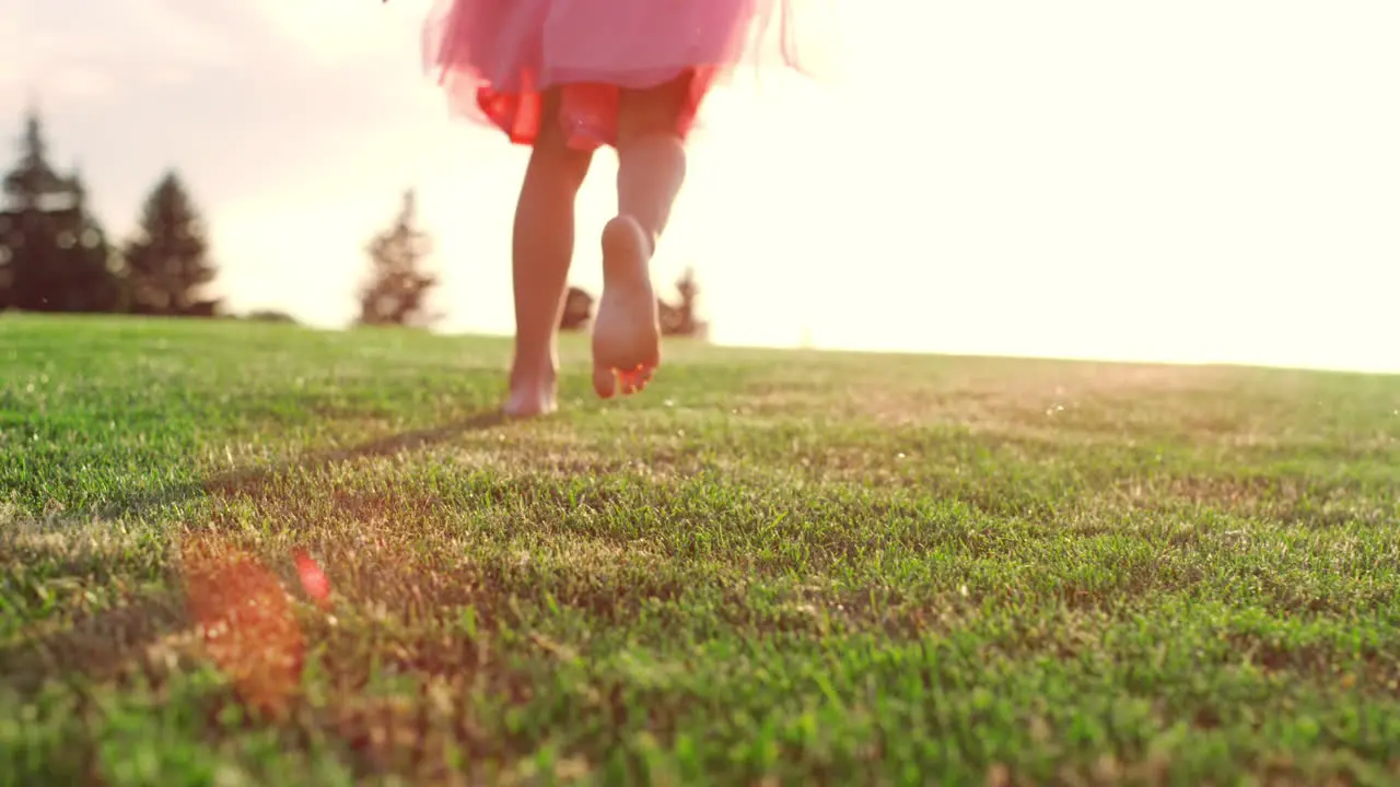 Unknown girl playing in city park Rear view of kid legs running on meadow