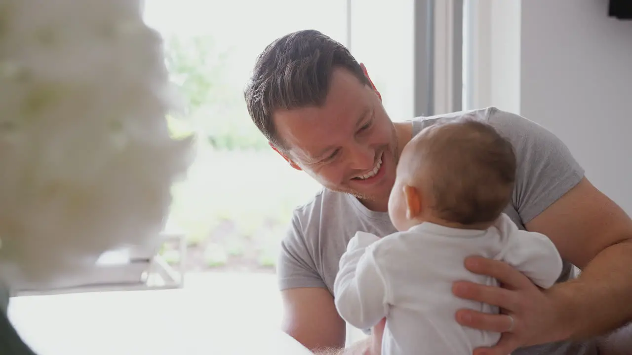 Loving Father Holding 3 Month Old Baby Daughter In Kitchen At Home Playing Game