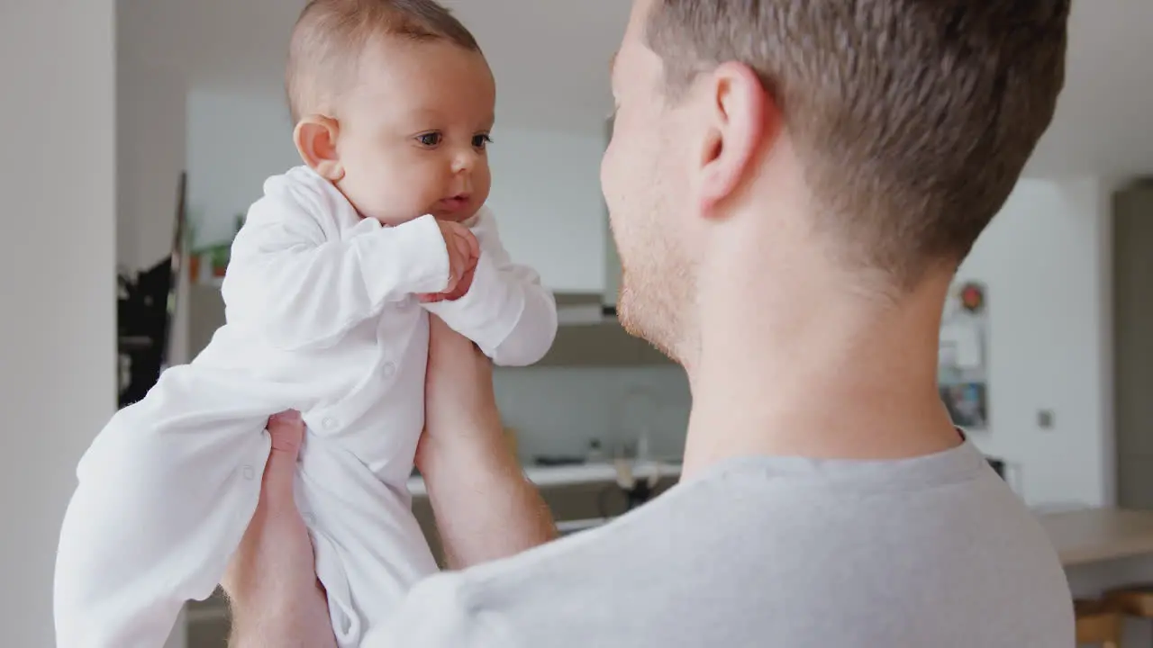 Loving Father Lifting 3 Month Old Baby Daughter In The Air In Kitchen At Home