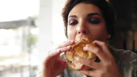 Close Up view of young woman biting big tasty burger in cafe Slow Motion shot