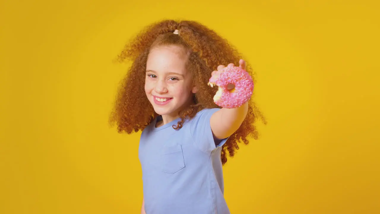 Studio Portrait Of Girl Eating Donut Against Yellow Background