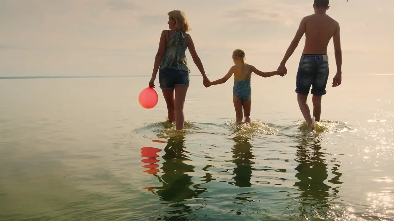 Mother And Childrens Walking On The Shallow Water At Sunset