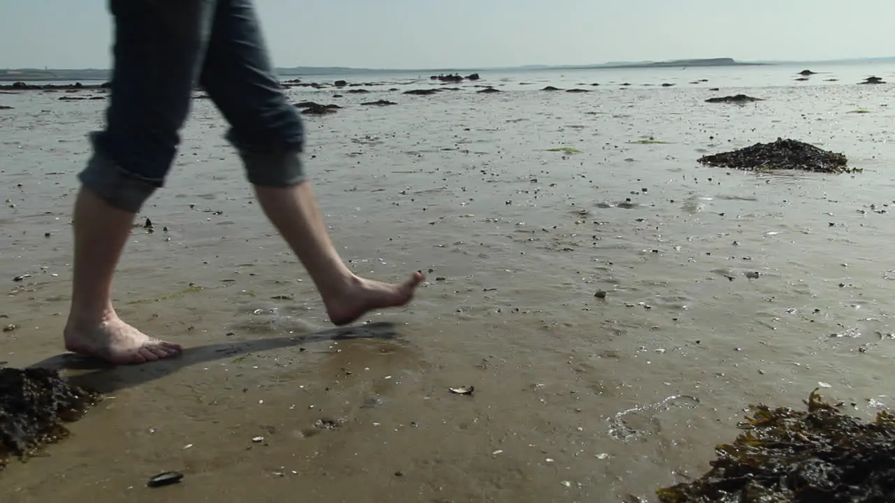 Man walking across wet beach bare foot at low tide