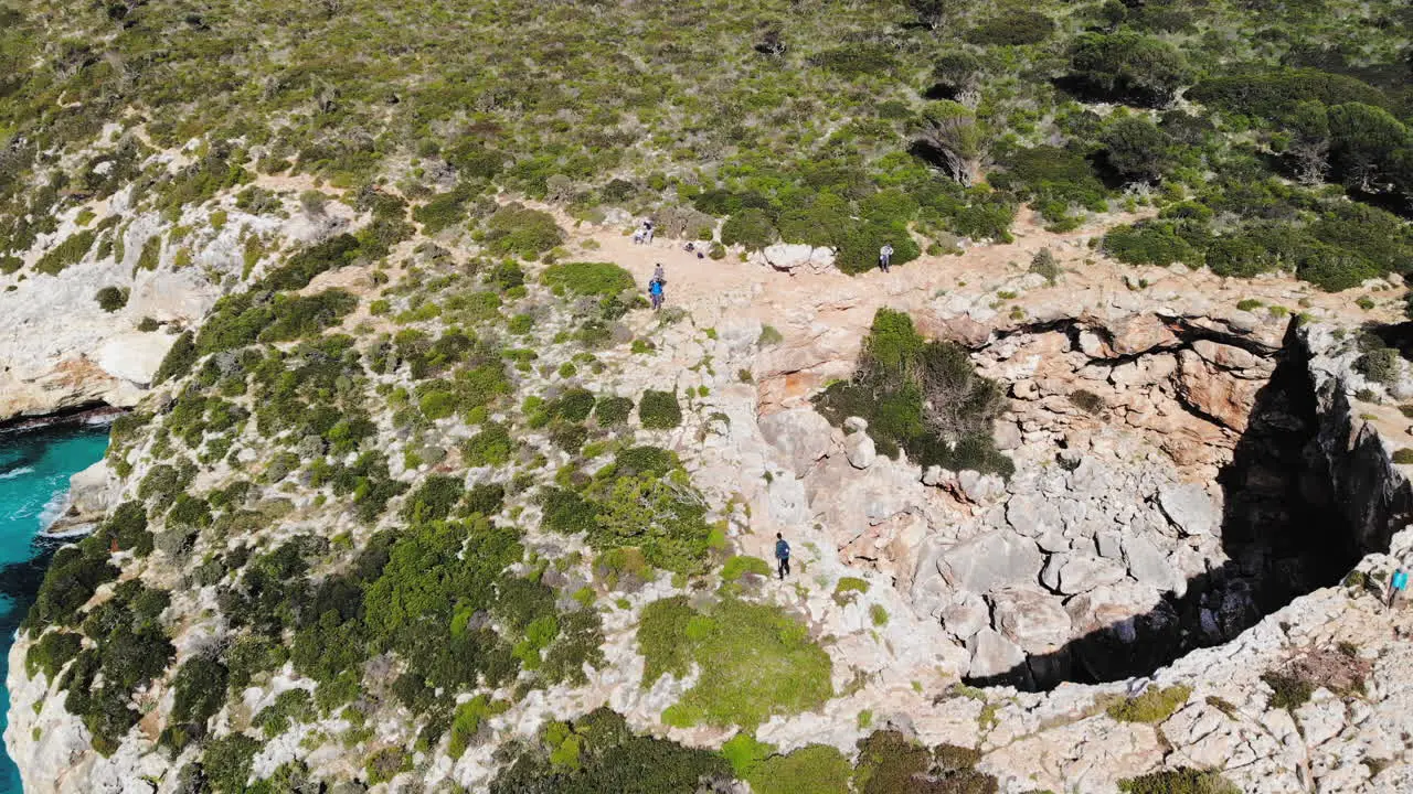 Backward flying drone shot over a sea arch with a few tourists walking around near Cala Varques beach in Majorca