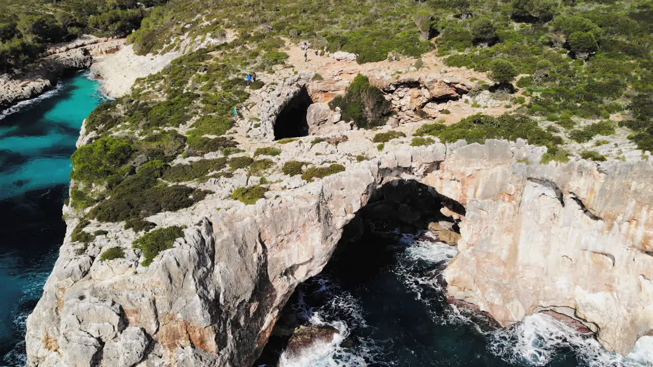 A forward flying drone shot towards a sea arch with tourists walking around near Cala Varques in Majorca