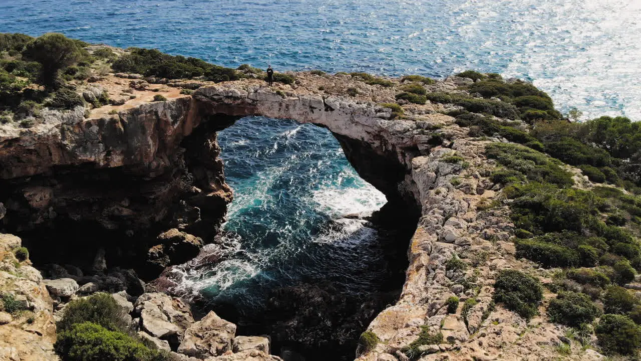 Still drone shot with tourists walking around in the distance at a sea arch near Cala Varques beach in Majorca