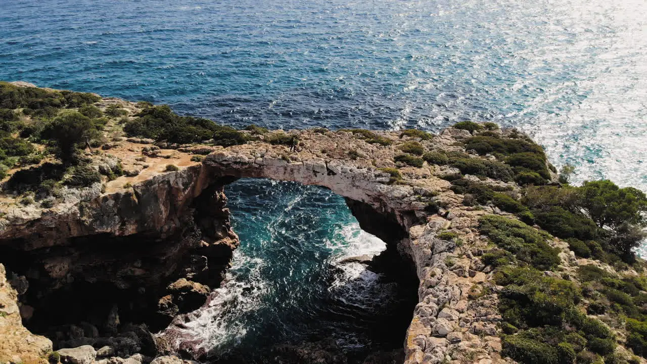 Upward flying drone shot of a sea arch with tourists walking