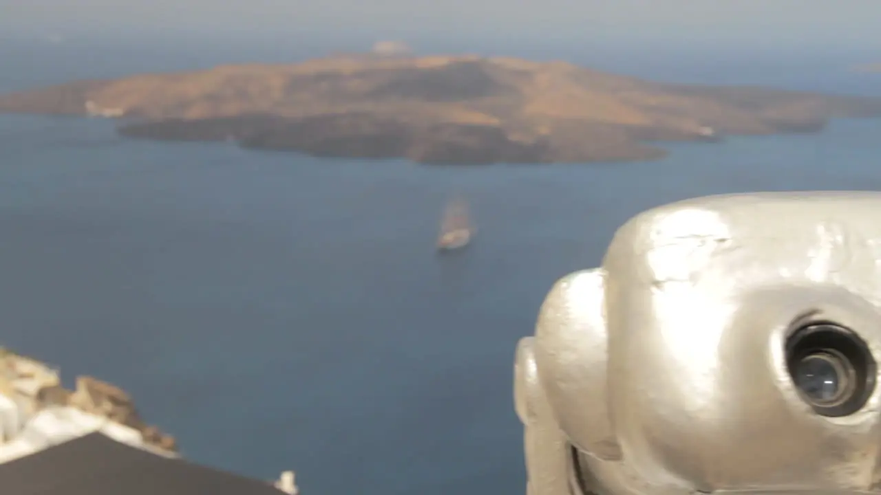 View of the volcanic island of Nea Kameni inside the Santorini Caldera as we track past a pair of public binoculars in close up