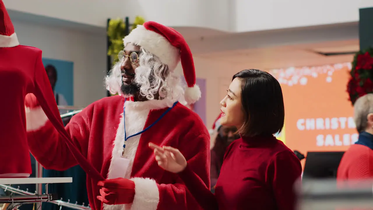 Retail assistant impersonating Santa Claus helping customer in shopping store find red blouse needed for Christmas party outfit Worker assisting woman in fashion shop during festive season