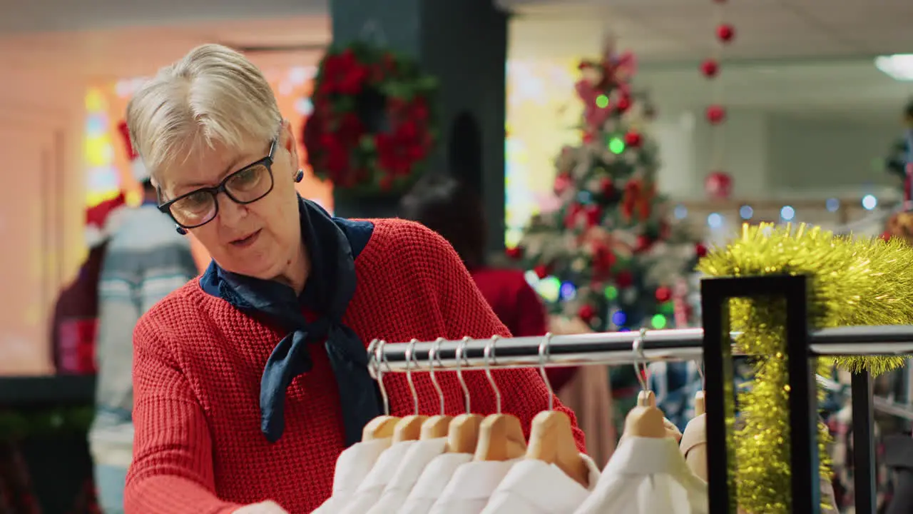 Elderly woman browsing through clothes in xmas adorn clothing store during winter holiday season Senior client in shopping spree session at Christmas decorated fashion boutique in mall