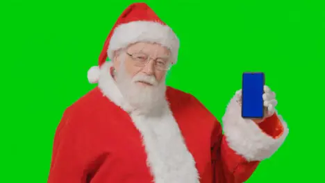 Portrait Shot of Santa Holding Blue Screen Mobile Phone In Front of Green Screen