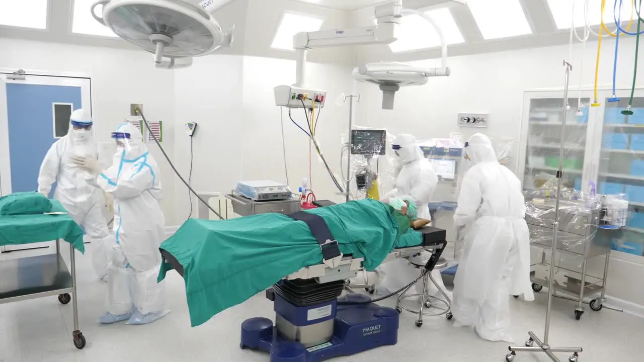 Asian Medical Staff Wear PPE Walk Into Operating Room With Patient On Operating Table