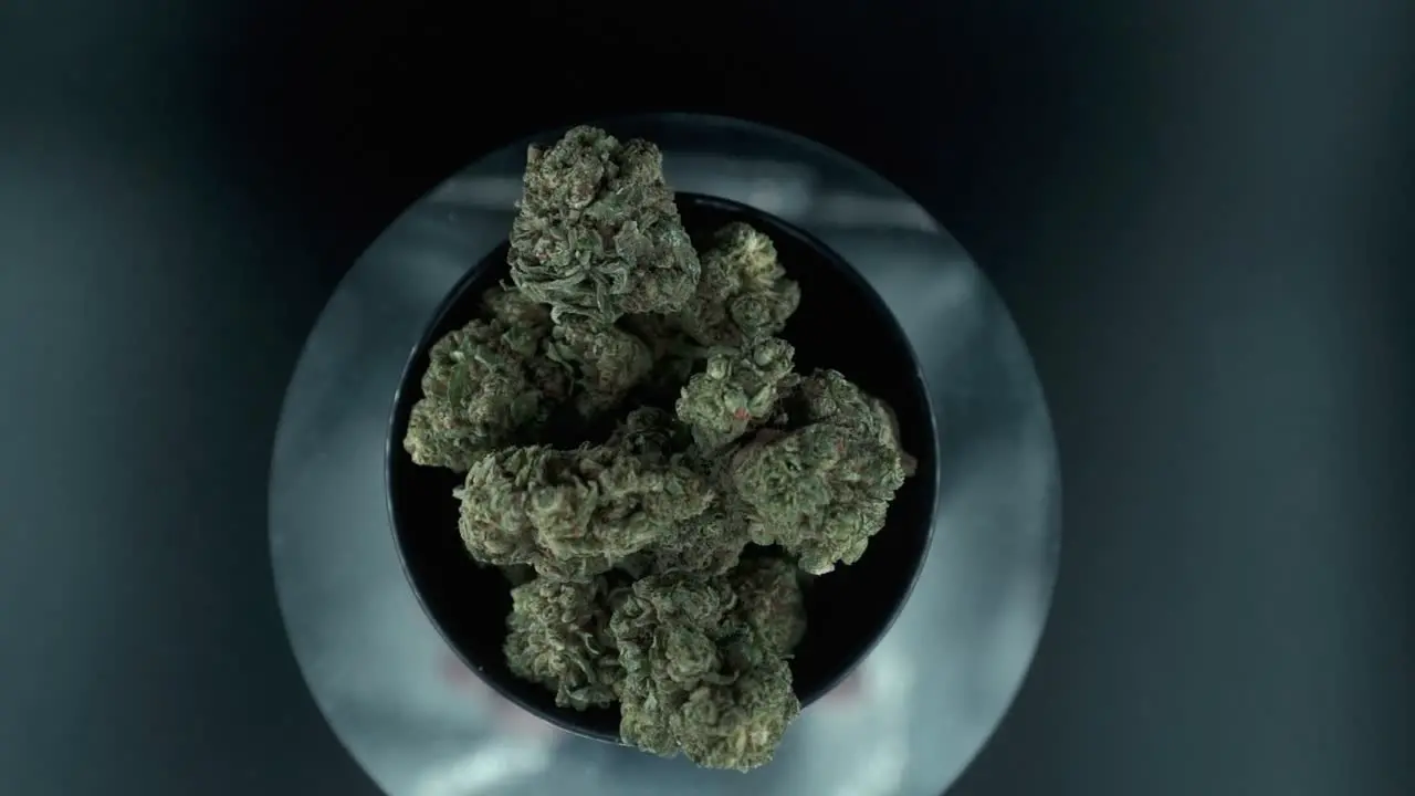 Grayish Green Dried Marijuana Buds view from above pile of dried marijuana plants in a shiny bowl trichomes strains on a reflecting rotating stand studio lights slow motion 120 fps zoom out