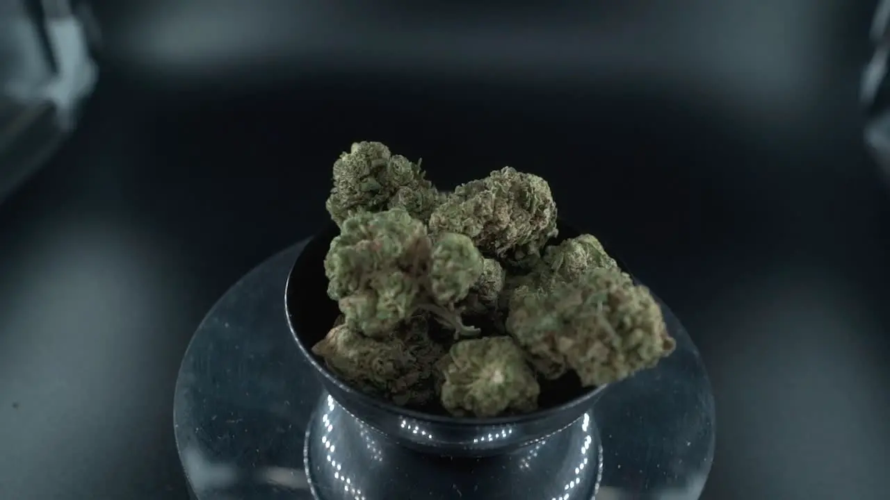 Green Dried Marijuana Buds Close Up Shot pile of dried marijuana plants in a shiny bowl trichomes strains on a reflecting rotating stand studio lights cinematic zoom out slow motion 120 fps