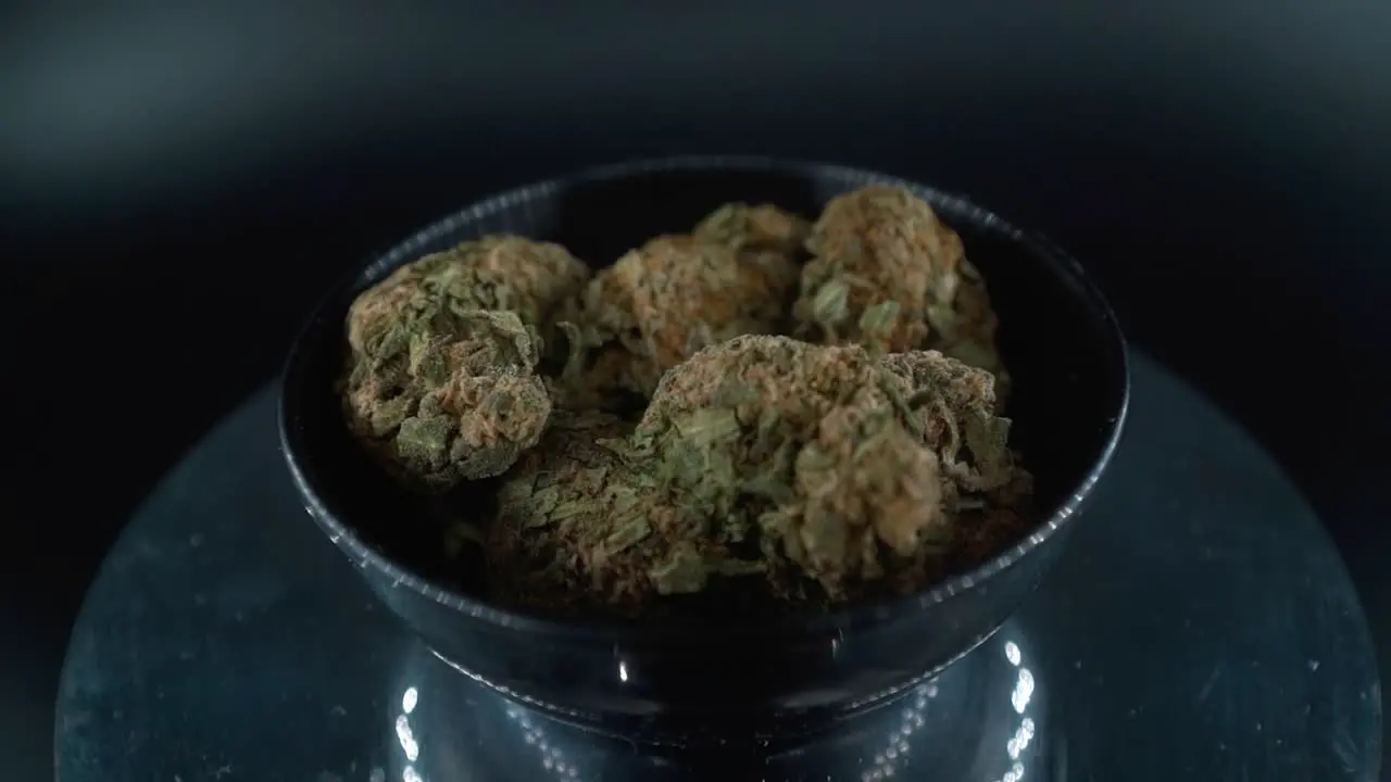 Dreamy Green Dried Marijuana Buds Close Up Shot pile of dried marijuana plants in a shiny bowl trichomes strains on a reflecting rotating stand studio lights cinematic crane rotating slow motion