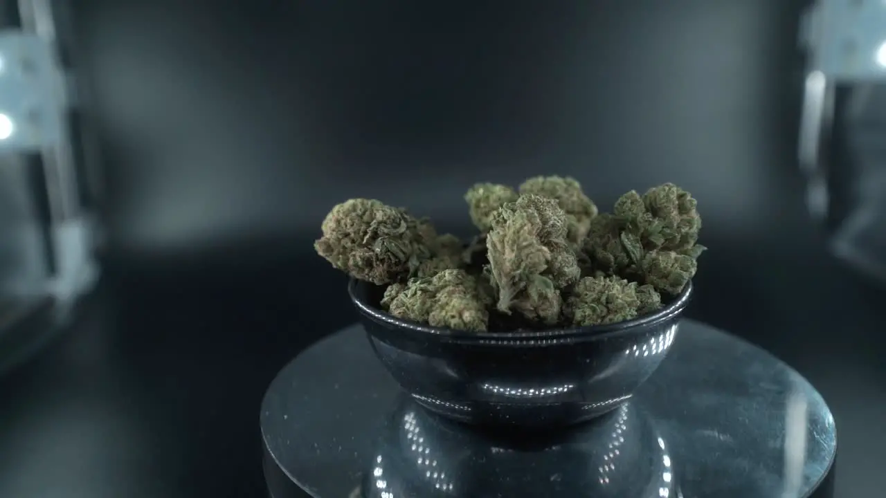 Green Dried Marijuana Buds Close Up Shot pile of dried marijuana plants in a shiny bowl trichomes strains on a reflecting rotating stand studio lights cinematic slow motion 120 fps follow right