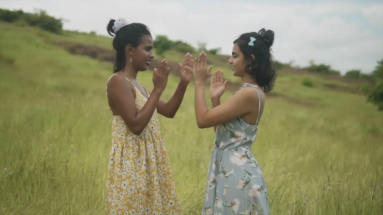 Wide angle on Two girls playing a hand clapping game in a countryside