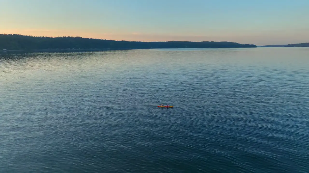 Aerial drone view circling left of two people in sea kayak paddling in a bay near seattle washington at sunrise revealing southworth community town