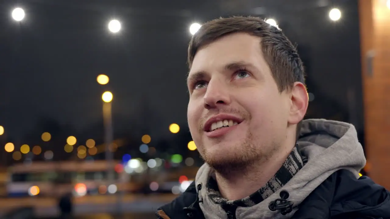 Young happy man smiling in city lights gazing up in closeup ant talking