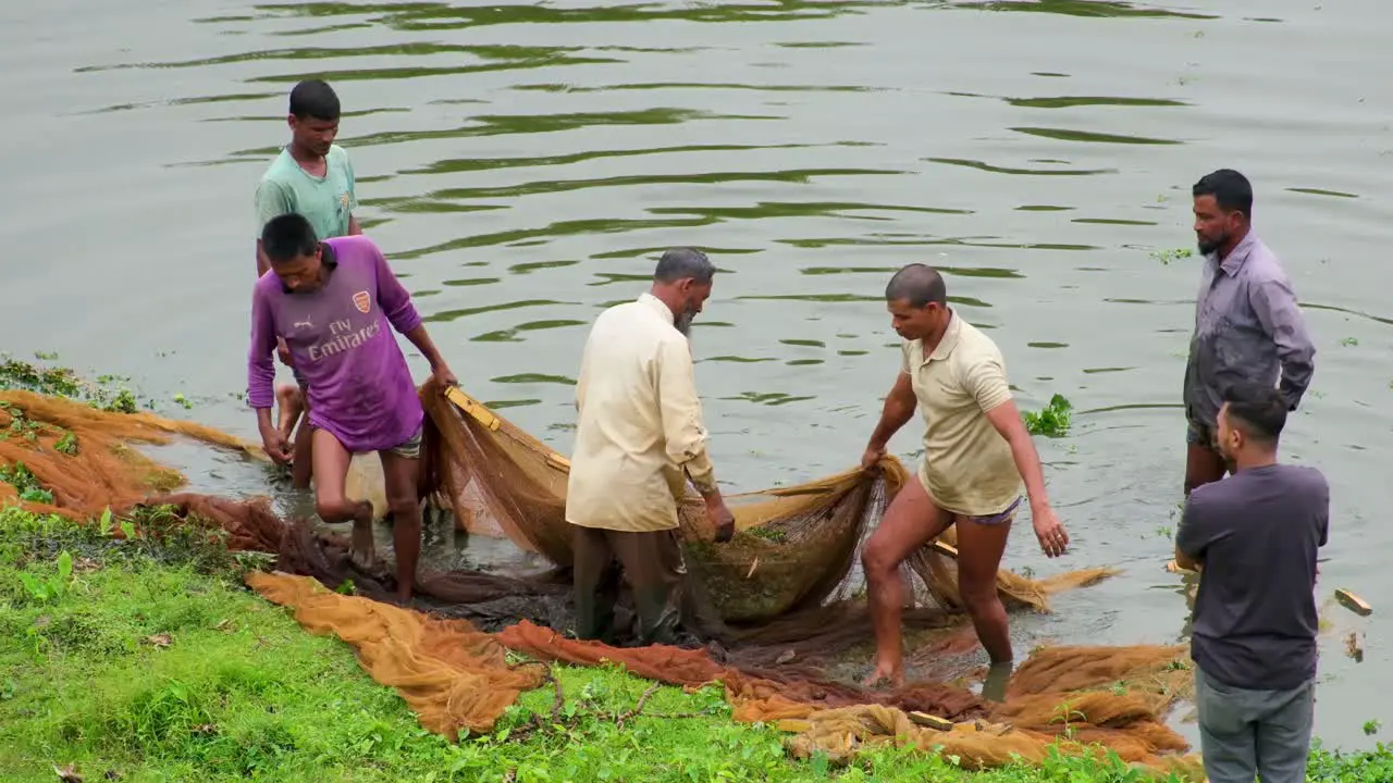 Group of Bangladesh fishermen on muddy riverbank drag in net full of fish