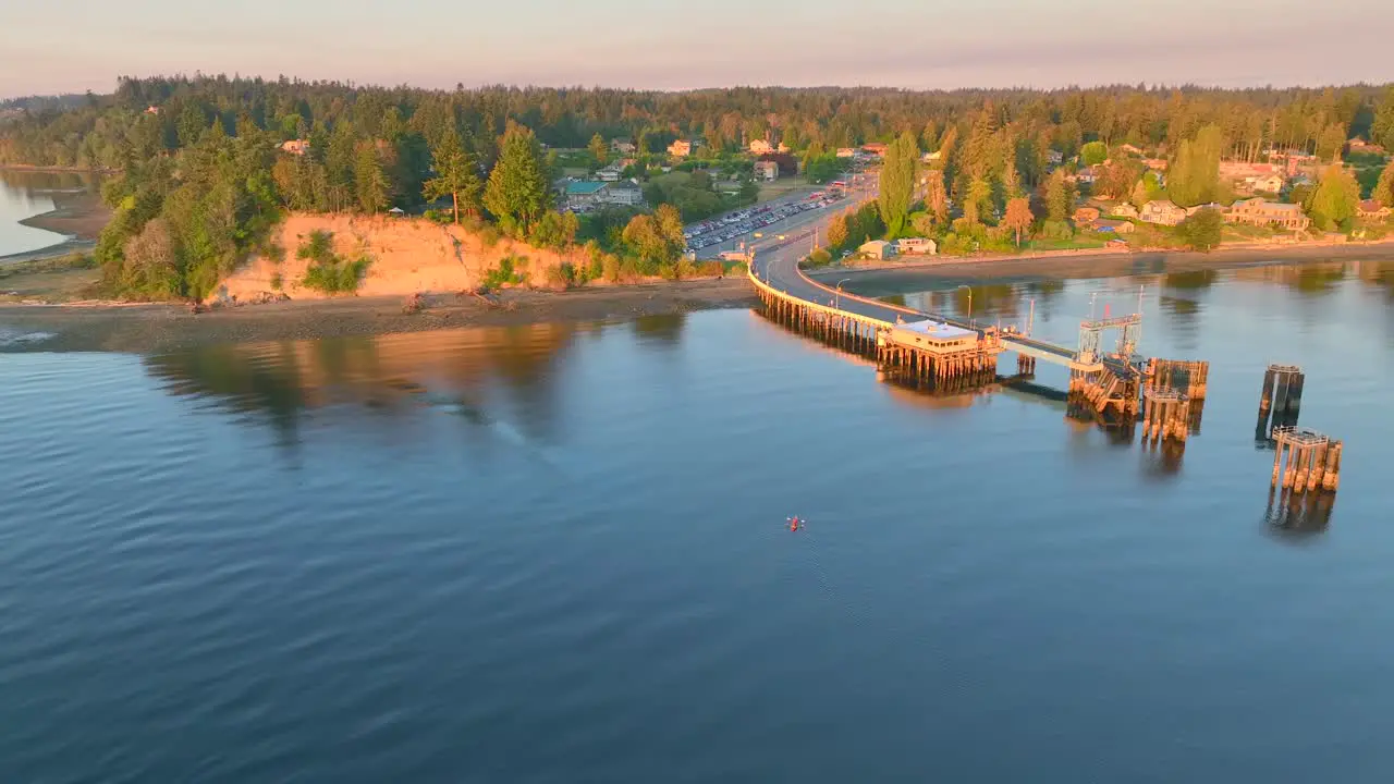 Aerial drone view circling left of two people in sea kayak paddling in a bay near seattle washington at sunrise revealing southworth community town and ferry terminal pier