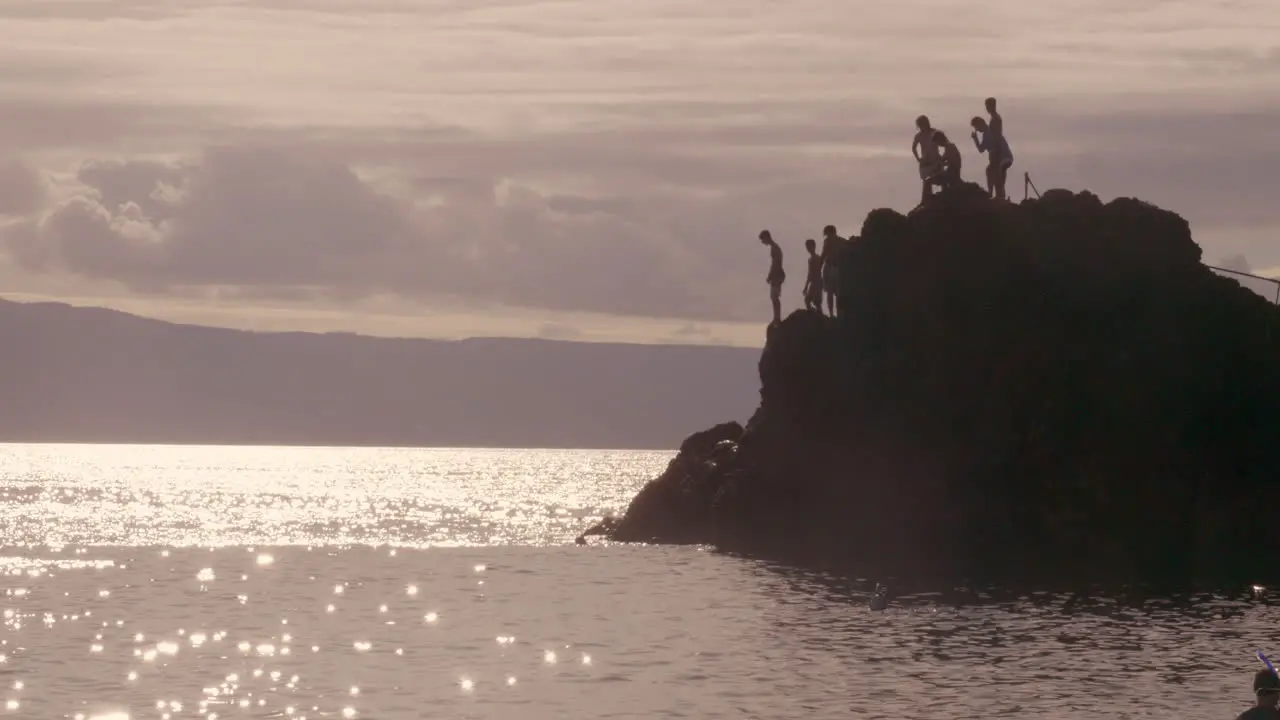 Shot of man jumping off cliff into the ocean during evening time