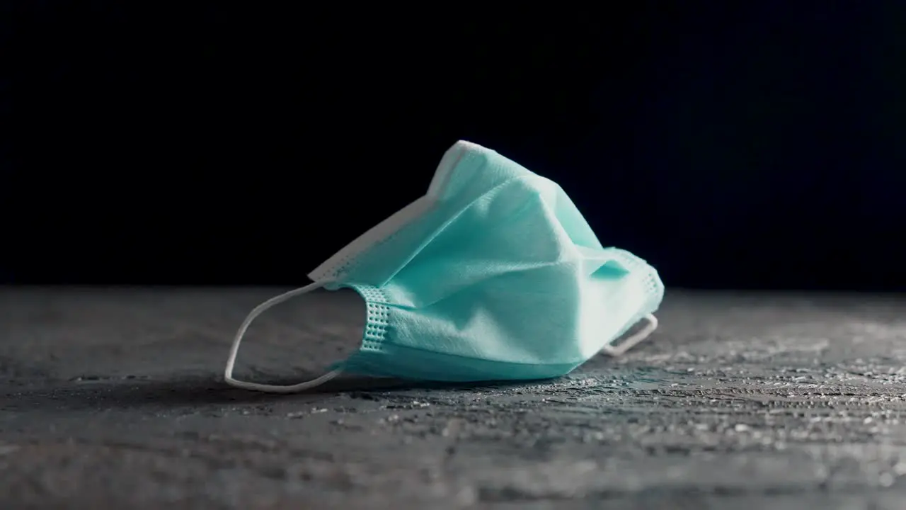 Blue surgical face mask in white on a table with black background filmed on a slider