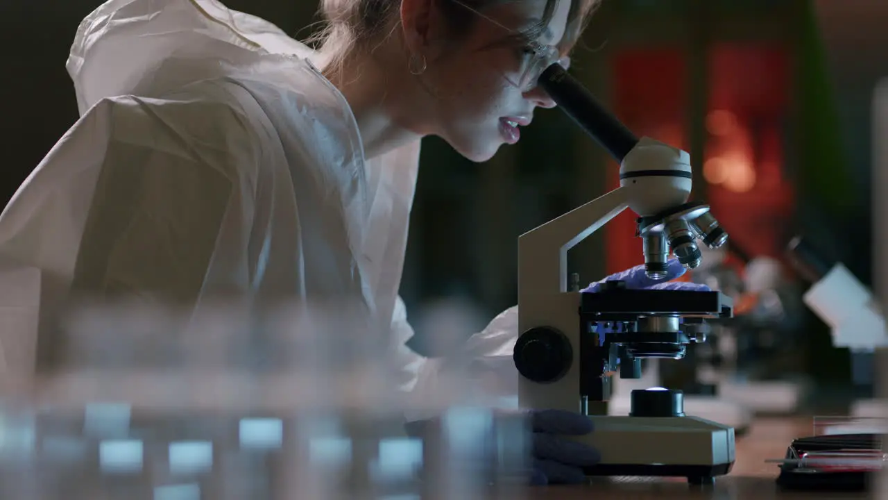 Female scientist with protective gear use microscope in laboratory