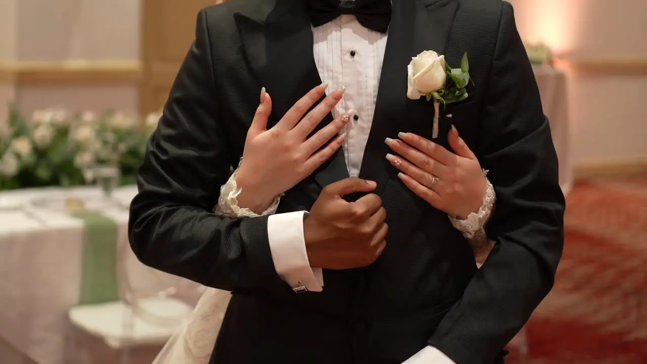 Groom in black wedding suit with his hands crossed and the bride's hands hugging each other from behind during the wedding ceremony