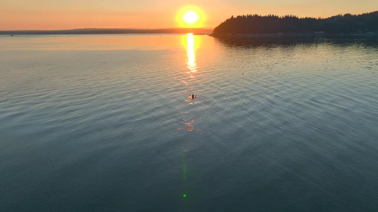 Aerial drone view of young couple paddling off into the sunset in a sea kayak in bay near seattle washington at sunrise