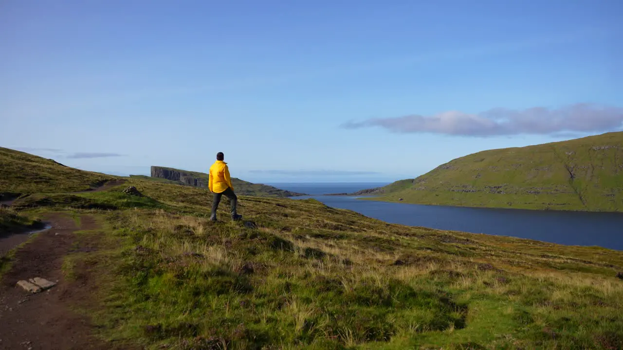 Man in yellow raincoat admiring the green and volcanic Faroese landscape in Leitisvatn