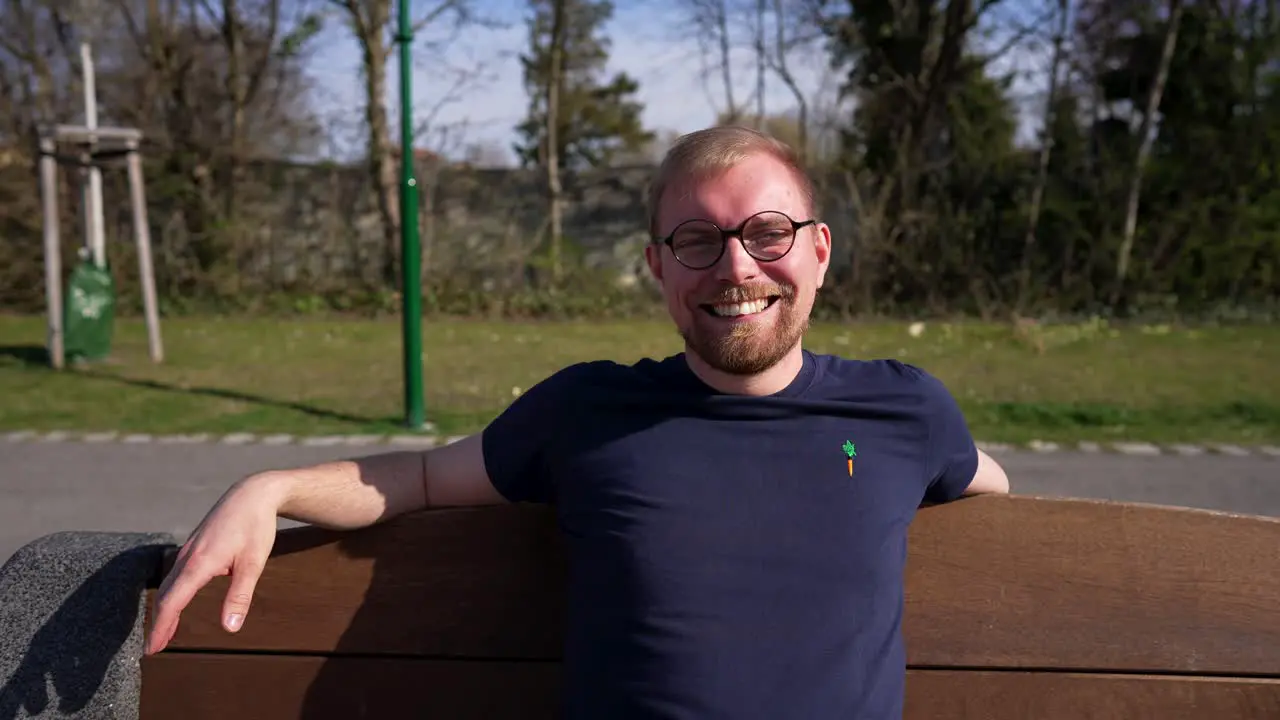 Caucasian Man Sitting on Outdoor Bench and Laughs Medium Parallax Shot