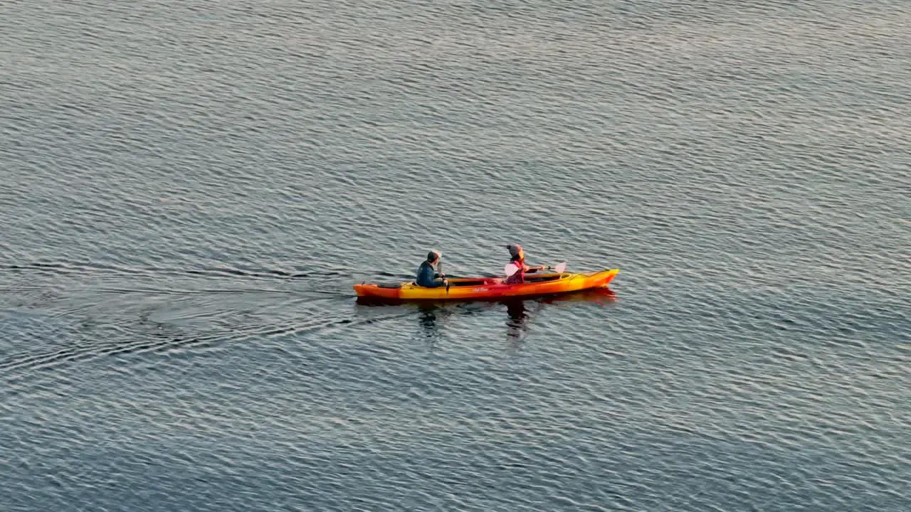 Close up aerial drone view of young couple having fun in a sea kayak paddling in a bay near seattle washington right after sunrise in the morning