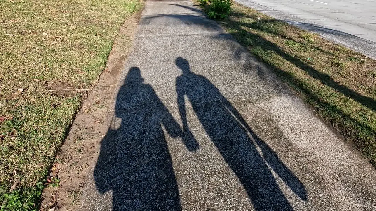 Unrecognizable shadow of an amorous couple holding hands as they walk projecting onto the sidewalk