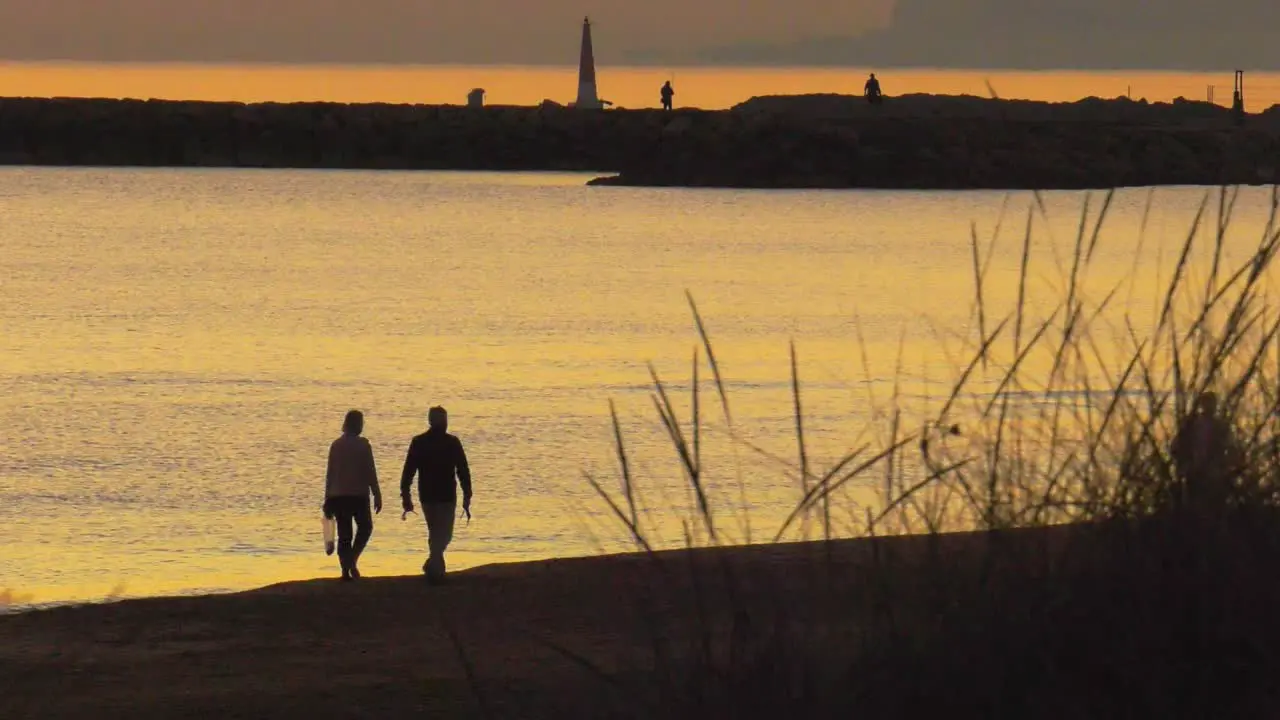 Older couple walking on beach together at dawn silhouette against calm sea slow motion