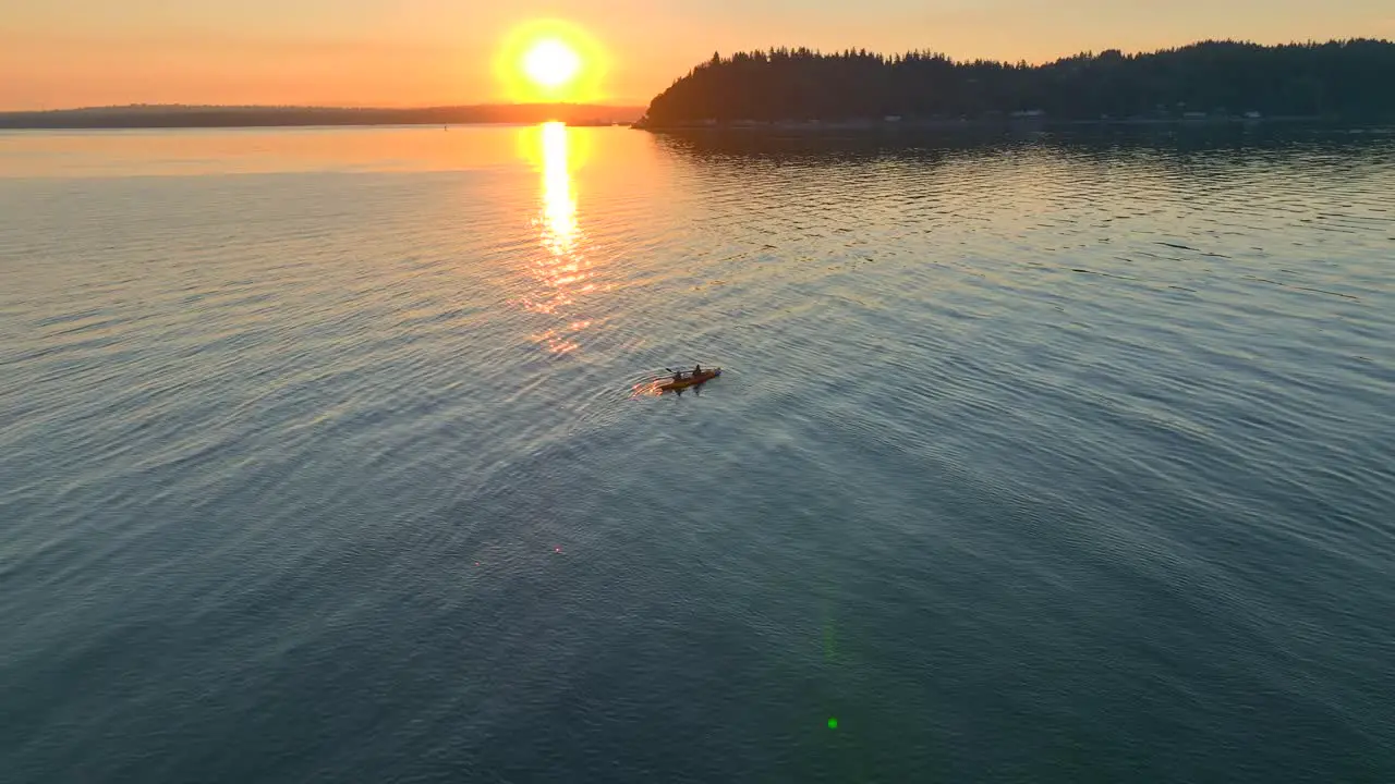 Aerial drone view fly in approach of young couple paddling off into the sunset in a sea kayak in bay near seattle washington at sunrise