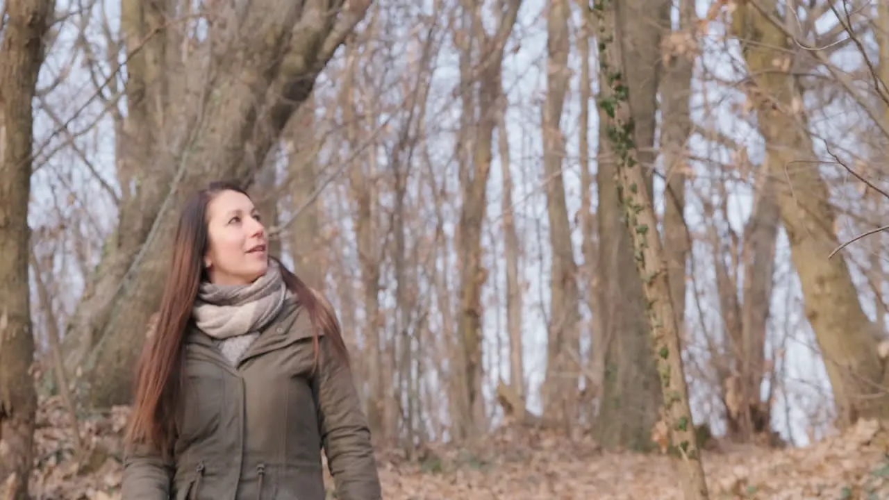 Brunette Woman Wearing Winter Jacket Walking In Forest And Looking Around On A Sunny Day