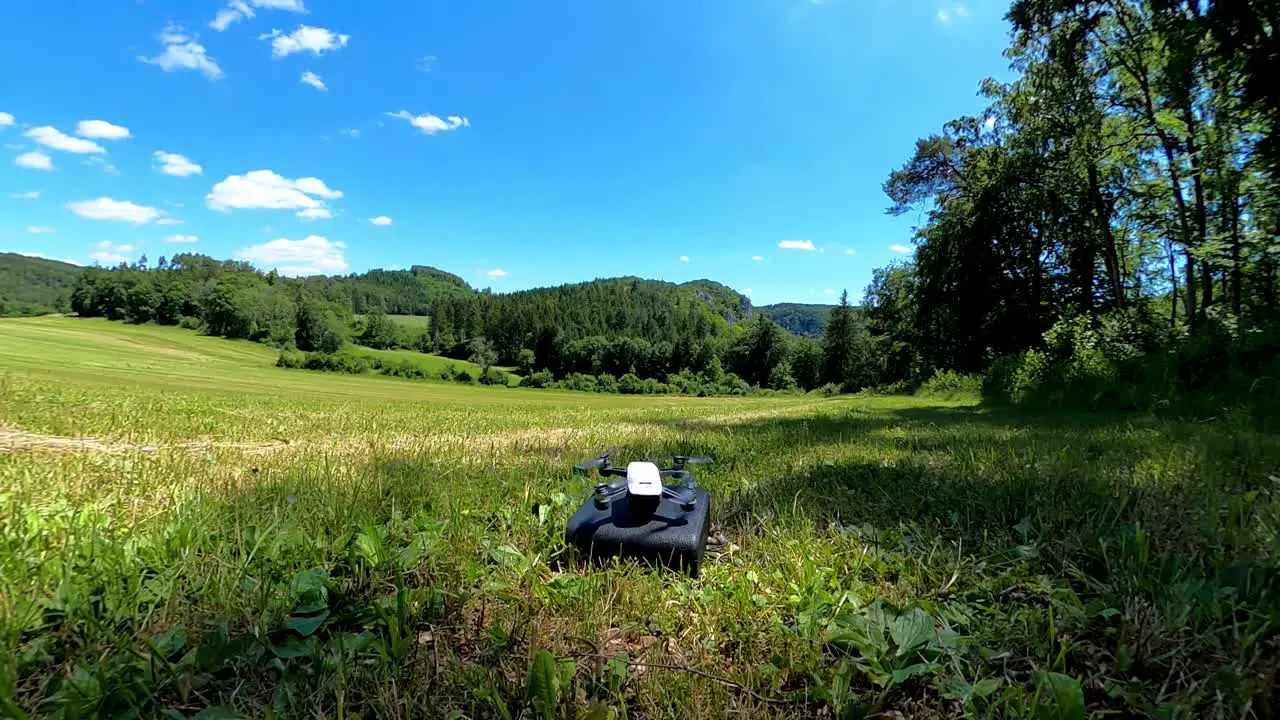 Small white drone with camera is taking off from black bag sunny day scenery in nature background with forest and grassy meadow