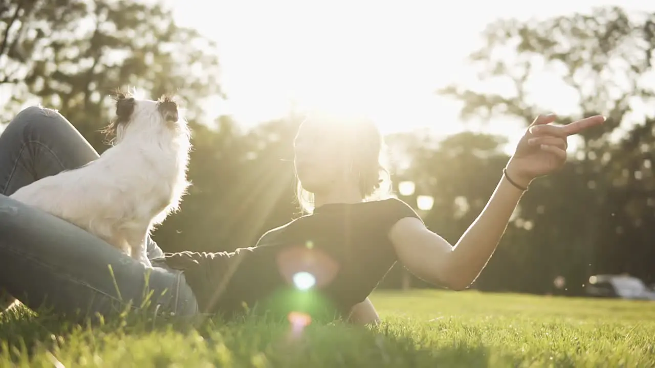 Cute Woman Lying On The Grass With Her Little Black And White Dog Sitting On Her Legs