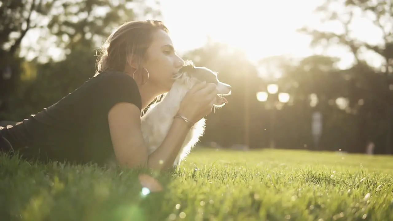 Side View Footage Of A Young Woman In Black T Shirt Lying On The Grass With Her Little Dog And Looking Straight Together Thoughtfully