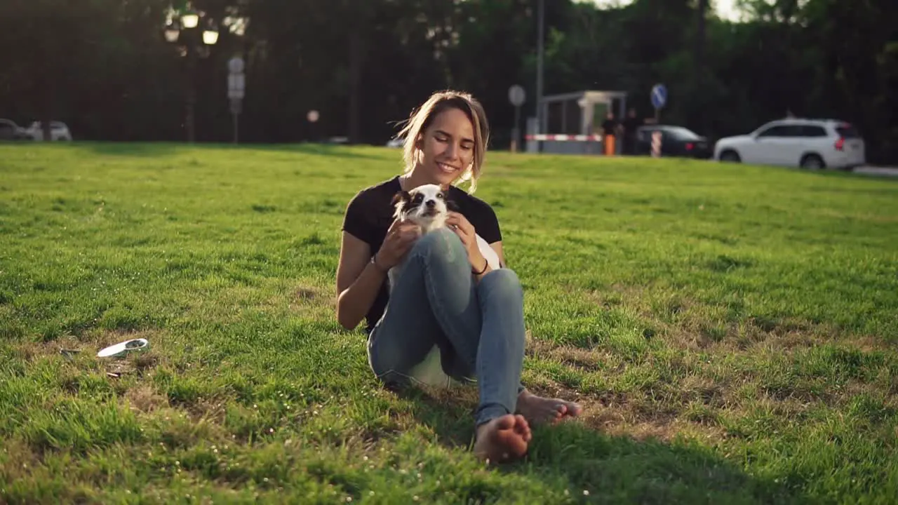 Beautiful Young Woman In Casual Sitting On Grass With Her Dog Pet And Smiling