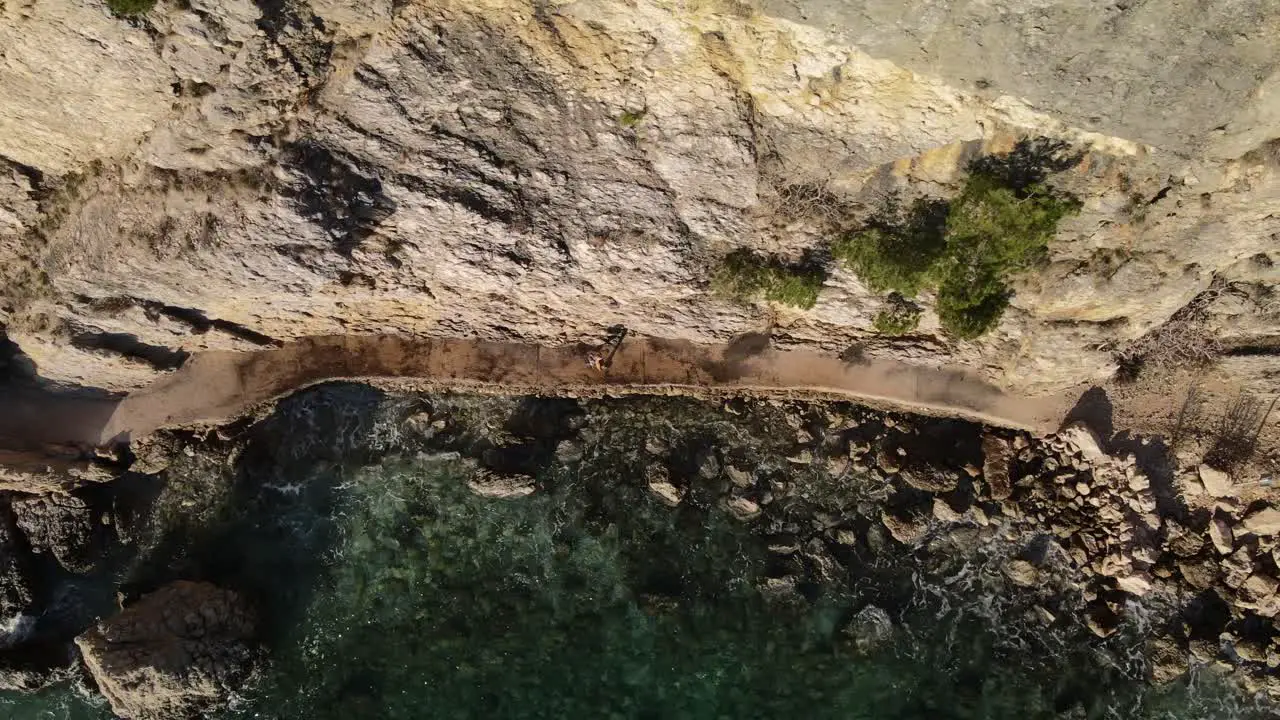 Aerial dolly shot overhead with drone on the coast of Beska in Croatia following a woman walking next to mountain in a sunny day