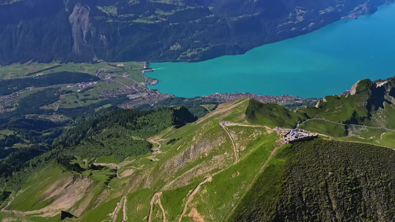 An aerial view of a green mountain range slowly revealing a turquoise lake and snow capped mountains in the background