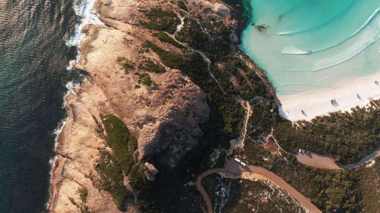 High-altitude top down drone trucking shot cliffs and rocks next to a beautiful white beach in Australia