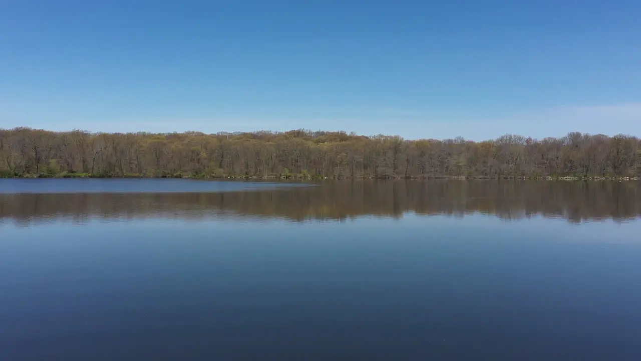 An aerial view of a blue reflective lake with bare trees lining the lake's edge